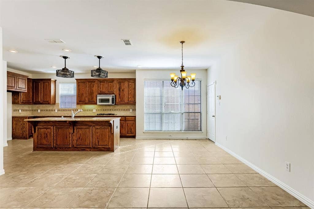 7013 Salem Court, Rowlett, TX 75089 Kitchen featuring wood cabinetry, a center island with a stone-finish countertop, tile flooring, dual pendant lighting, and a multi-arm chandelier