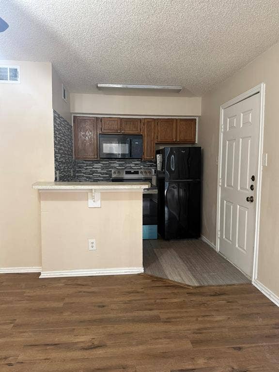 Kitchen featuring a pass-through breakfast bar, wood-finish cabinetry, a textured stone-pattern backsplash, and wood-finish flooring