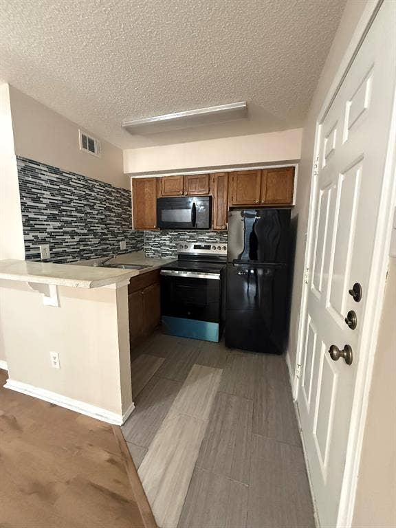 Kitchen featuring wood cabinetry, a mosaic-tile backsplash, black appliances, and a pass-through breakfast bar with stone-finish countertops
