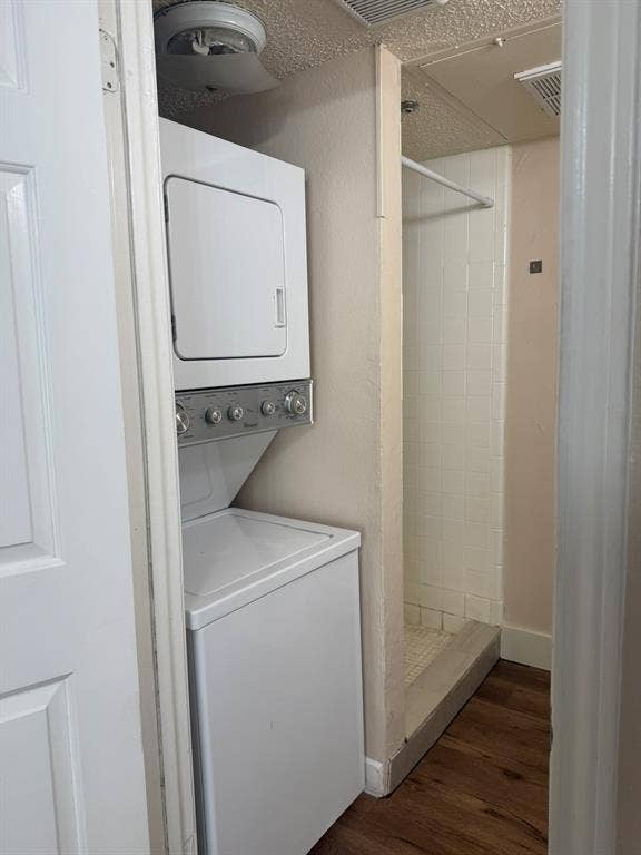 Stacked laundry center featuring a white washer and dryer, tile-surround shower, and wood-finish flooring