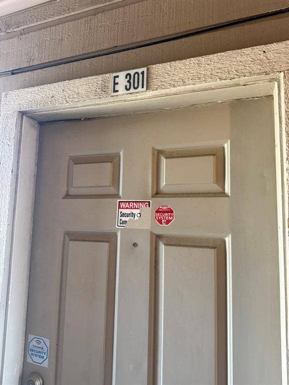 Entry door featuring a six-panel design and a door-mounted peephole, positioned beneath a unit number identification plaque