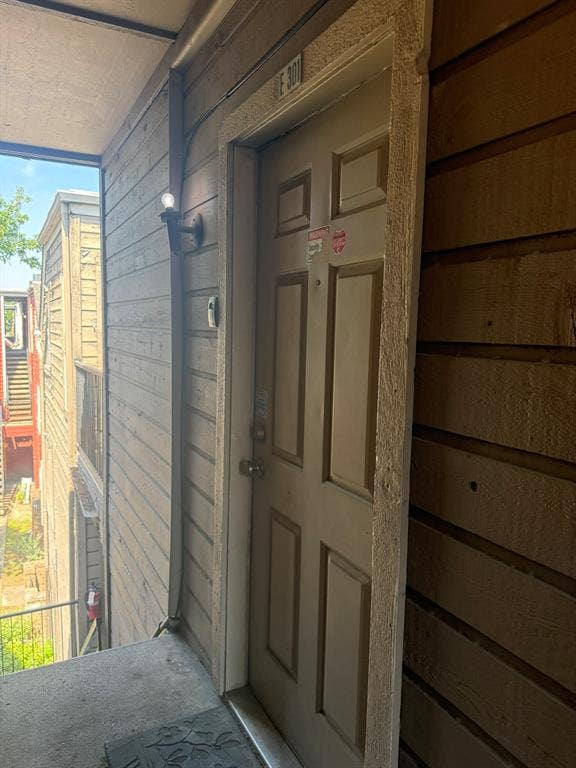 Exterior entry featuring a six-panel door, horizontal wood-finish siding, and an attached wall-mounted light fixture