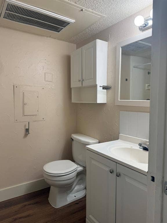 Bathroom featuring a vanity with an integrated sink, white cabinetry, wall-mounted storage cabinet, framed mirror, and wood-finish flooring