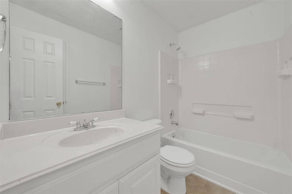 Bathroom featuring a white vanity with an integrated sink, a large wall-mounted mirror, a porcelain tub with a tiled surround, and a chrome faucet fixture