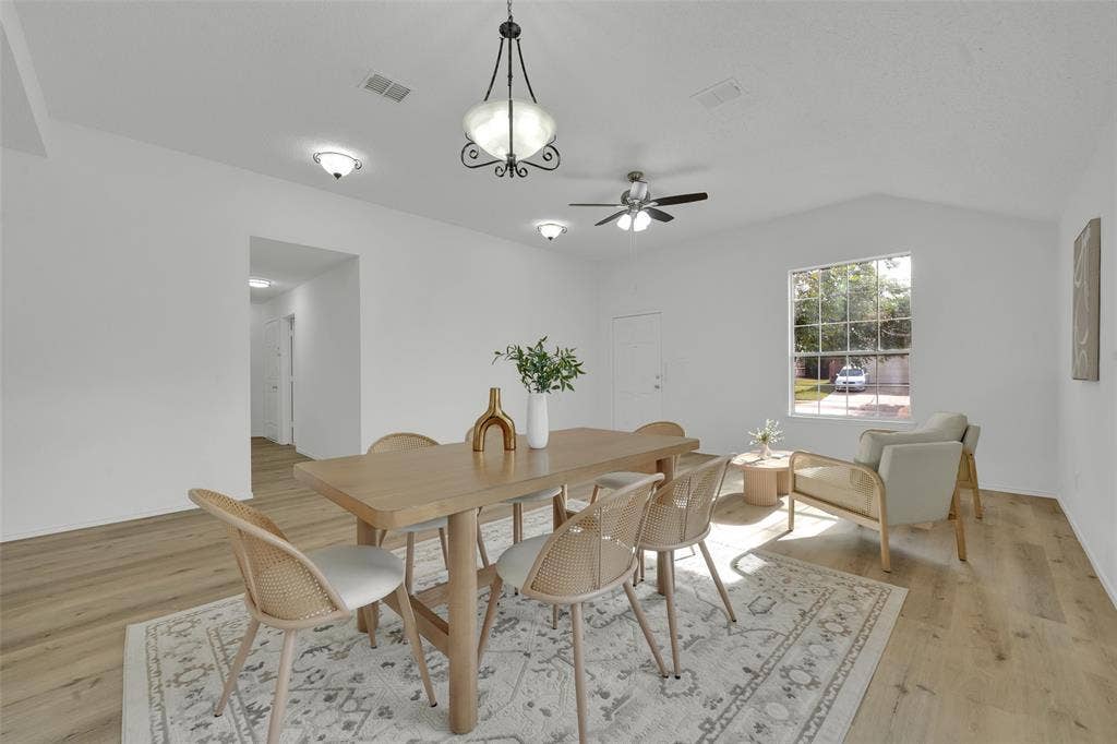Open-concept area featuring light wood-finish flooring, vaulted ceilings, a multi-light chandelier, a ceiling fan with integrated lighting, and a multi-pane window