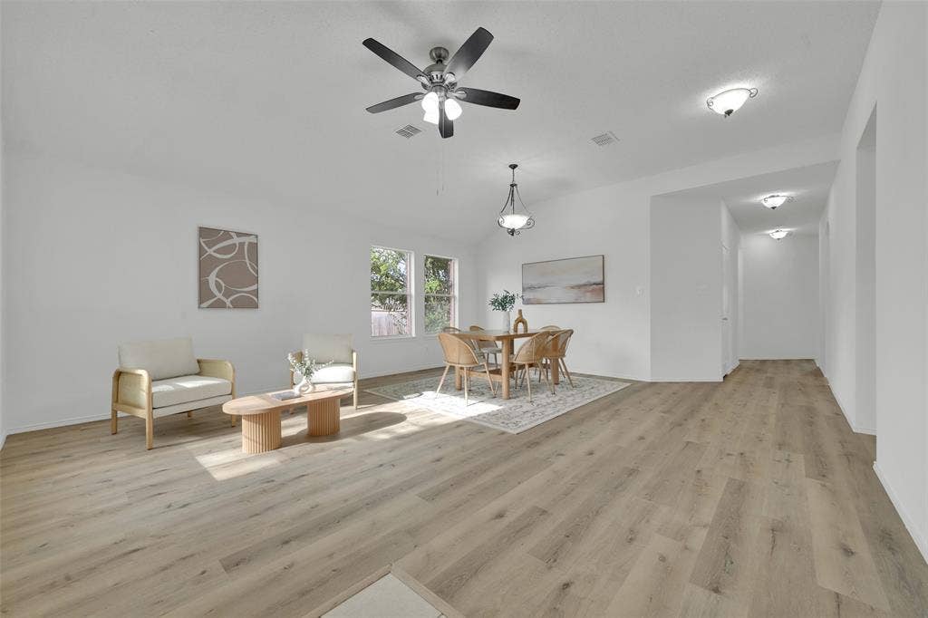 Open-concept area featuring wood-finish flooring, vaulted ceilings, a central ceiling fan with integrated lighting, and multiple hanging light fixtures