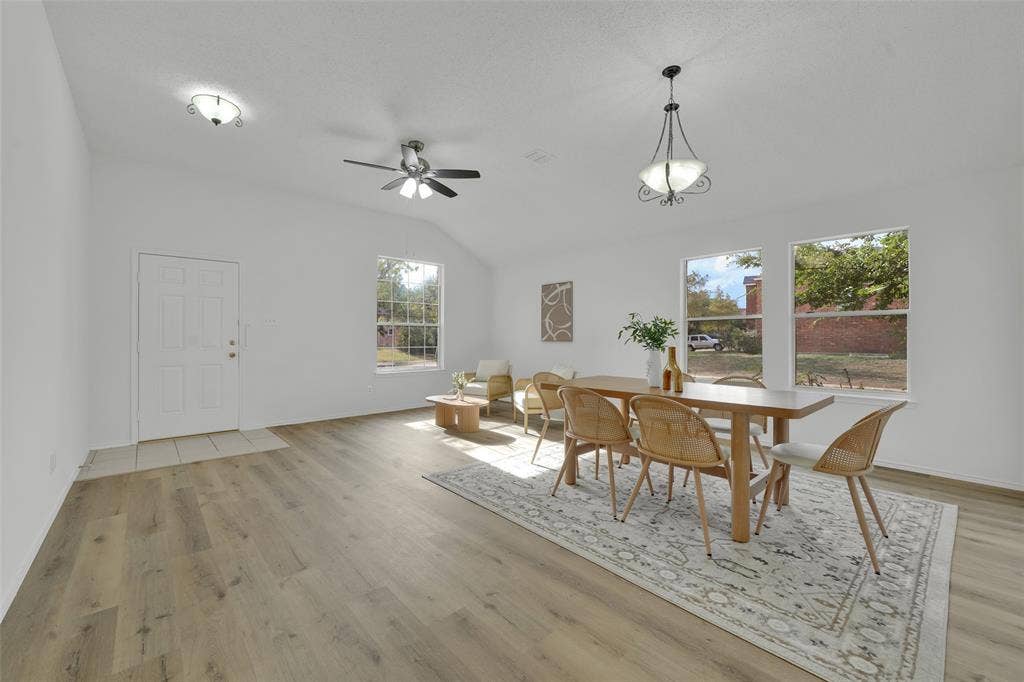 Open-concept interior featuring wood-finish flooring, vaulted ceilings, multi-pane windows, a central ceiling fan, and a decorative pendant light fixture