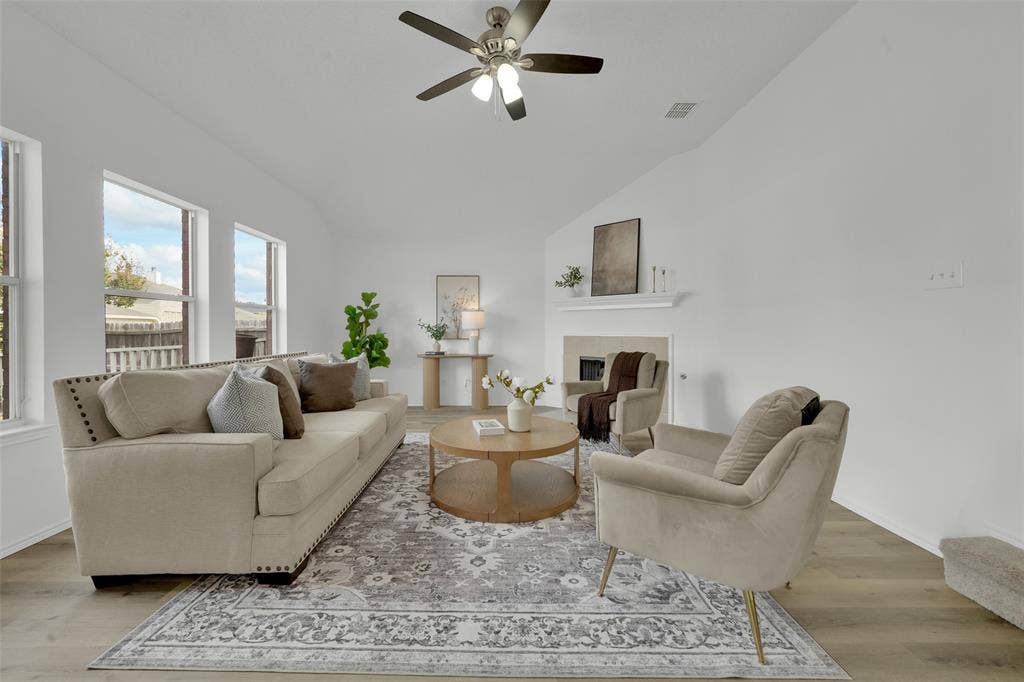 Living area featuring vaulted ceilings, wood-finish flooring, a fireplace with a mantel, and multiple tall windows
