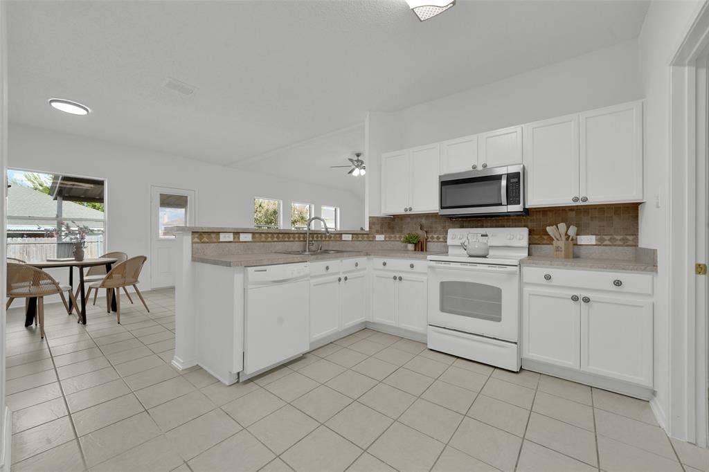 Kitchen featuring white shaker-style cabinetry, neutral-toned tiled flooring, stone-finish countertops, tile backsplash, and stainless steel microwave