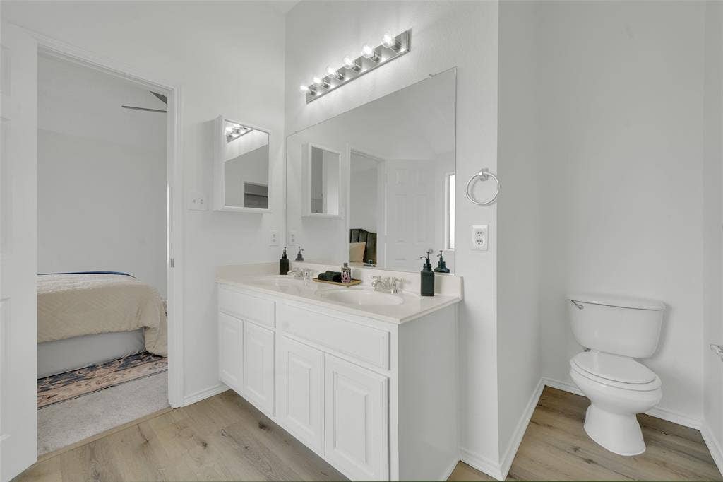Double vanity featuring white cabinetry, integrated dual sinks, countertop with a neutral finish, expansive wall-mounted mirror, and multi-bulb light fixture
