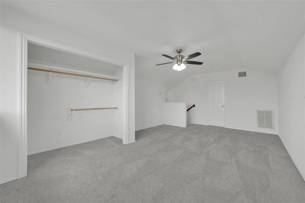 Neutral-toned wall-to-wall carpeting, open-concept closet with dual tiered hanging rods, multi-blade ceiling fan with integrated light fixture, and six-panel interior door