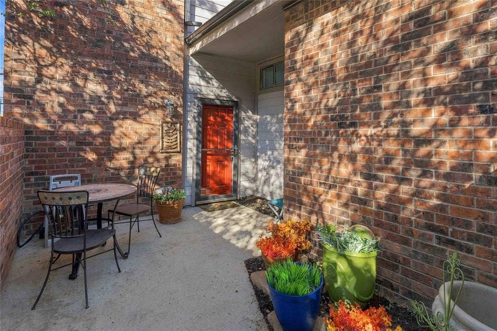 18240 Midway Road, #1706, Dallas, TX 75287 Courtyard entrance featuring a red paneled front door, brick exterior walls, and a concrete patio floor