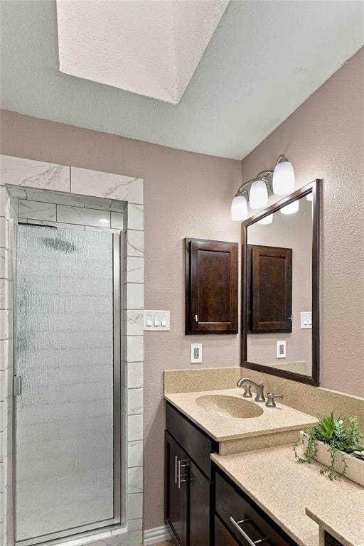 18240 Midway Road, #1706, Dallas, TX 75287 Bathroom featuring a shower stall with tile surround, skylight, built-in dark wood cabinetry, solid surface countertop with integrated basin, and a framed vanity mirror with three-light fixture