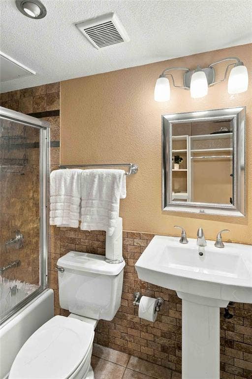 18240 Midway Road, #1706, Dallas, TX 75287 Pedestal sink with polished metal faucet, glass-enclosed shower with tiled surround, and three-light wall-mounted fixture