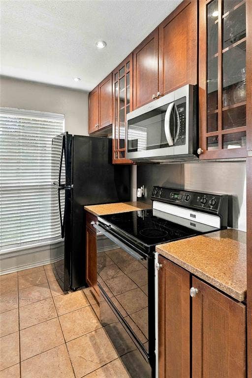 18240 Midway Road, #1706, Dallas, TX 75287 Kitchen featuring wood cabinetry with glass-paneled uppers, stone-finish countertops, tile flooring, and stainless steel microwave