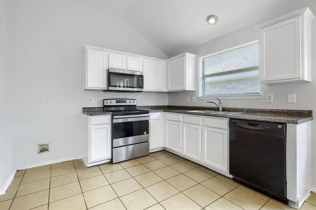 Open-concept space featuring vaulted ceilings, tile flooring, white cabinetry, and stainless steel appliances