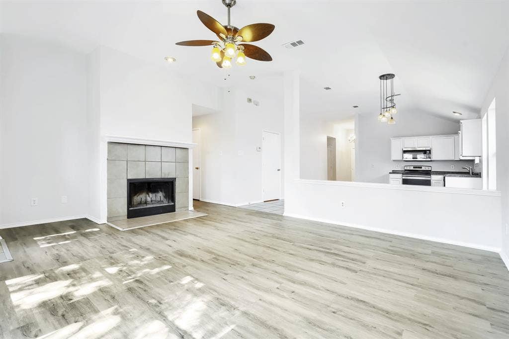 Vaulted ceilings, wood-finish flooring, tile-surround fireplace, and ceiling fan with integrated lighting