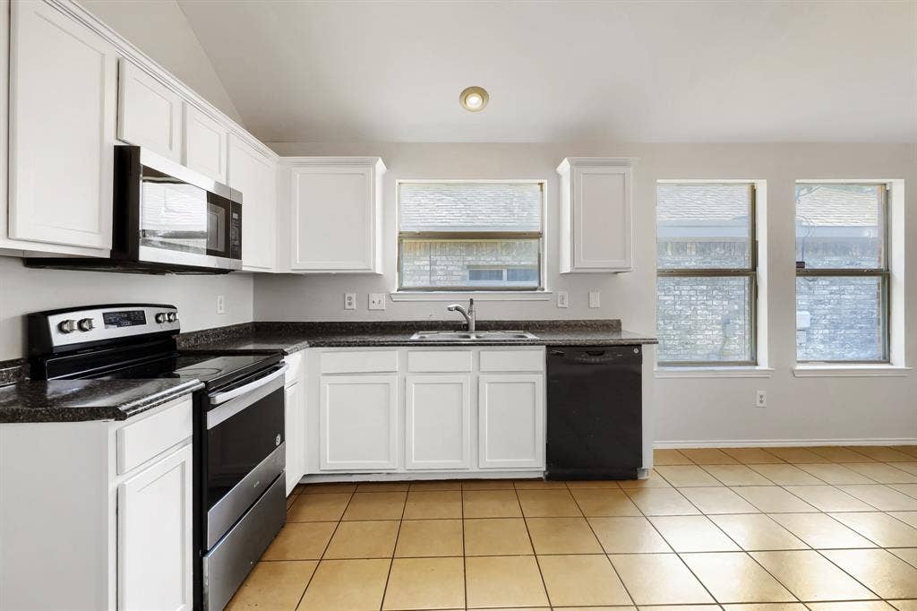 Kitchen featuring white shaker-style cabinetry, stone-finish countertops, stainless steel appliances, ceramic tile flooring, and a vaulted ceiling