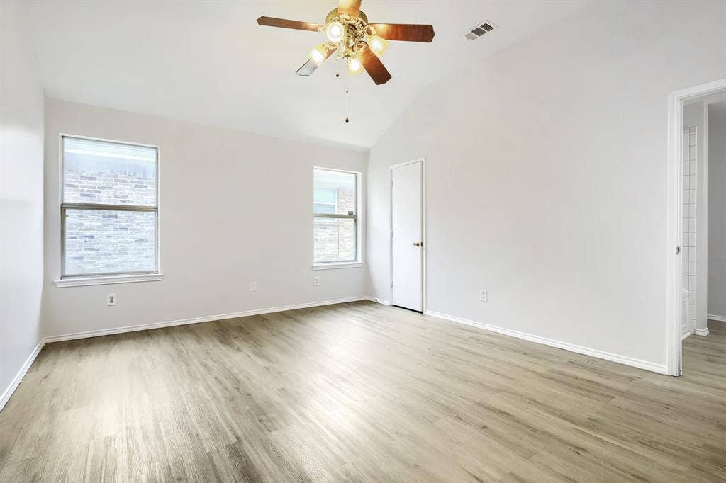 Neutral interior room featuring wood-finish flooring, high ceilings, and a central ceiling fan with multi-light fixture