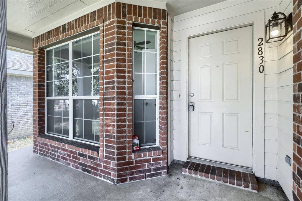 Covered entry featuring a brick-accented exterior, multi-pane windows, a paneled door, and an exterior wall-mounted light fixture