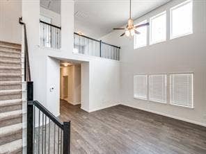 Double-height ceiling, wood-finish flooring, staircase with a metal balustrade, upper-level mezzanine, and multi-pane windows