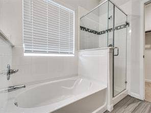 Oval soaking tub, separate glass-enclosed shower, polished chrome fixtures, white tile surround, and wood-finish flooring