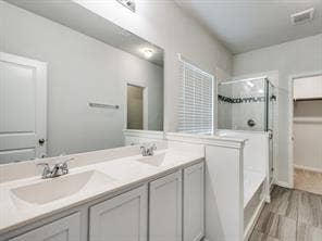 Dual vanity with rectangular under-mount sinks, expansive wall-mounted mirror, glass-enclosed shower, and wood-finish flooring