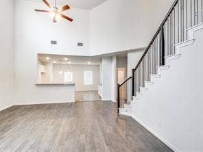 Two-story height ceiling with overhead fan, wood-finish flooring, staircase featuring dark metal balusters and a wood handrail, and built-in pass-through opening