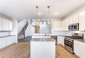 Kitchen featuring white shaker-style cabinetry, a central island with countertop seating, stainless steel appliances, pendant lighting, and wood-finish flooring