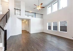 Expansive two-story room featuring vaulted ceilings, wood-finish flooring, large windows, a ceiling fan, and a metal-railed staircase