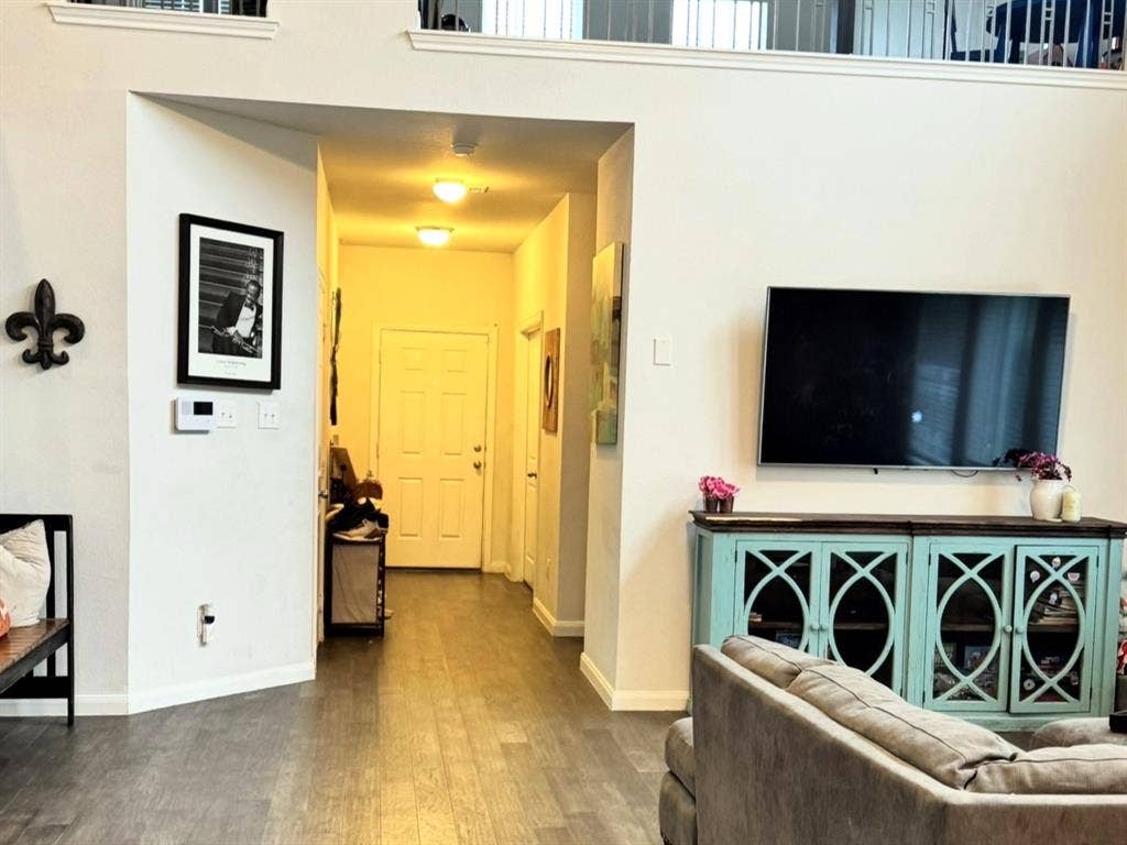 High-ceiling living area featuring wood-finish flooring and a mezzanine balcony with metal railing