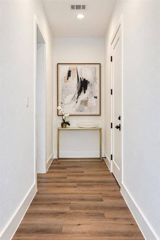Recessed ceiling lighting, wood-finish flooring, white walls, white trim, and a white door with black hardware