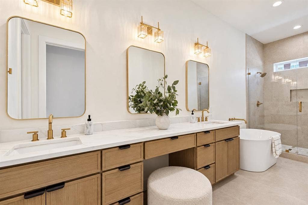 Double vanity with integrated sinks, wood-finish cabinetry, gold-tone hardware, and a freestanding soaking tub