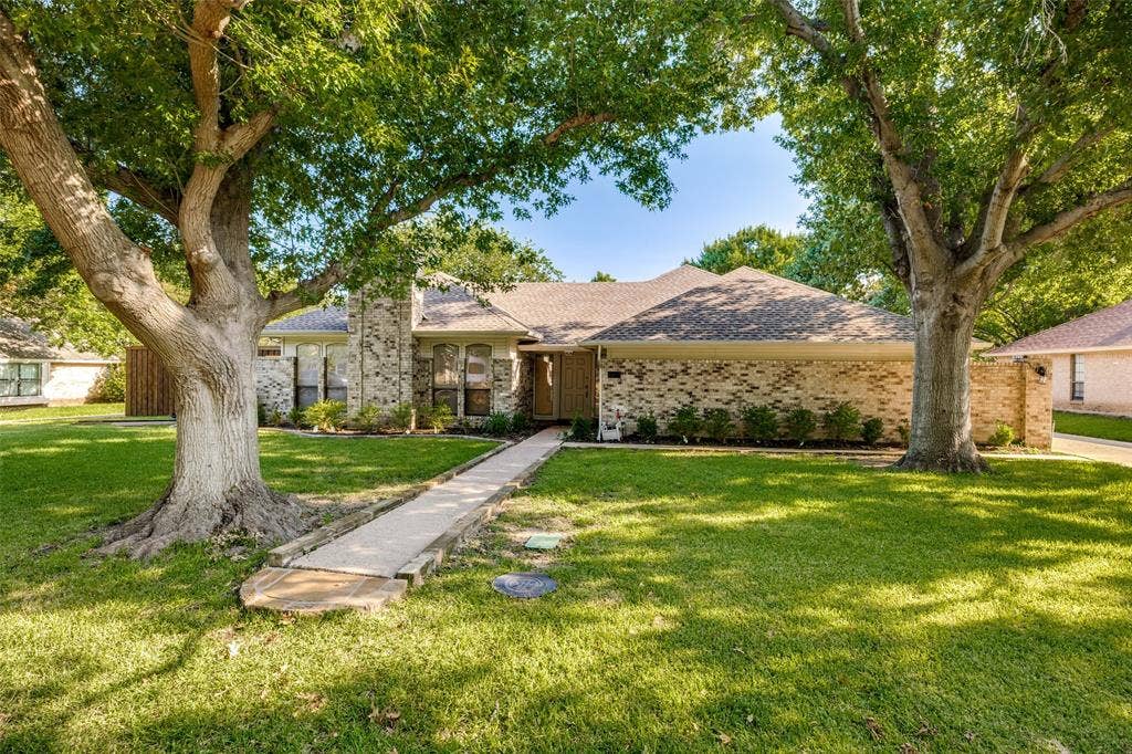 6627 Sawmill Road, Dallas, TX 75252 Single-story brick exterior featuring a multi-gabled roofline, concrete walkway, and expansive front lawn with mature trees