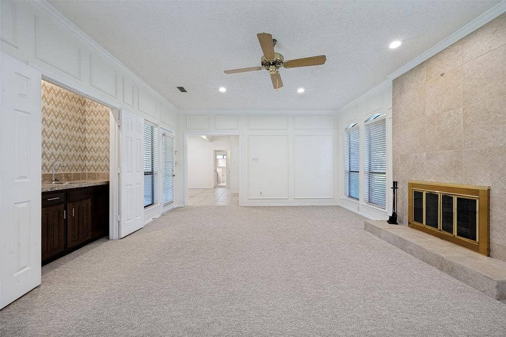 6627 Sawmill Road, Dallas, TX 75252 Living area featuring floor-to-ceiling stone fireplace surround, custom wall paneling, built-in wet bar with cabinetry, and recessed lighting