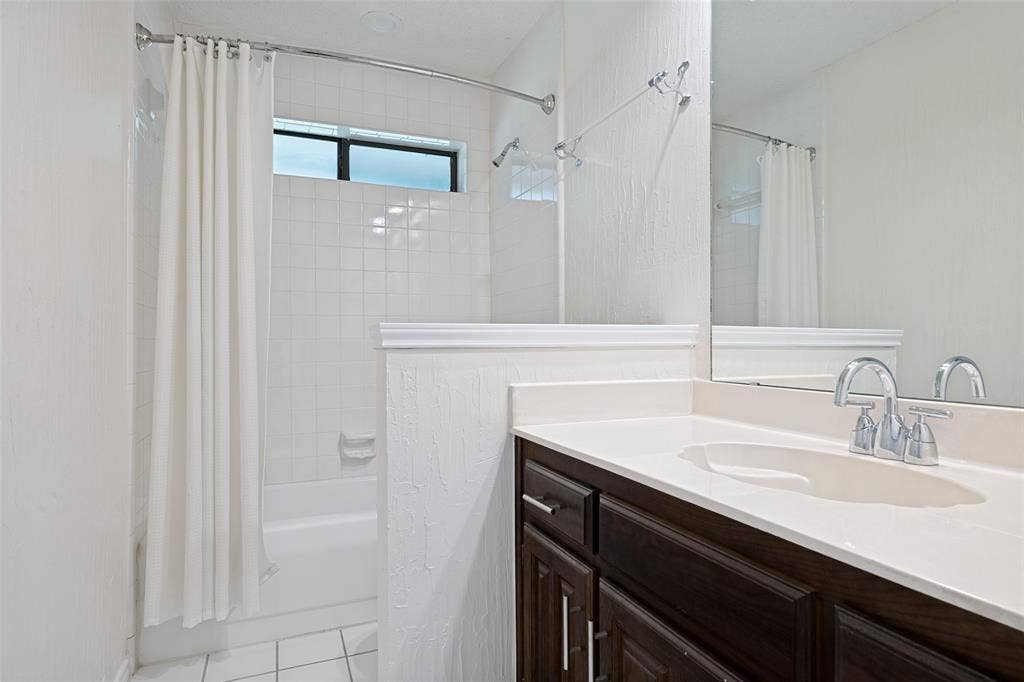 6627 Sawmill Road, Dallas, TX 75252 Dark wood-finish vanity with a white countertop, integrated sink, polished chrome faucet, and a wall-to-wall mirror