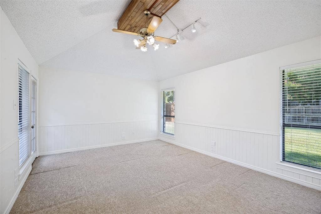 6627 Sawmill Road, Dallas, TX 75252 Vaulted ceiling featuring a wood-beam accent, beadboard wainscoting, carpeted flooring, track lighting, and multiple windows with horizontal blinds