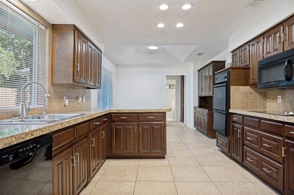 6627 Sawmill Road, Dallas, TX 75252 Kitchen featuring dark wood cabinetry, stone countertops, tiled backsplash, integrated double wall ovens, and recessed lighting