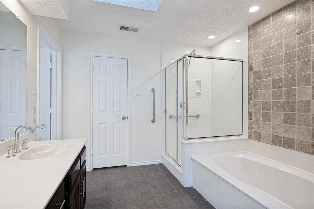 6627 Sawmill Road, Dallas, TX 75252 Bathroom featuring a dark wood-finish vanity with a light-toned countertop, a glass-enclosed shower, a deep soaking tub with a tiled accent wall, and recessed lighting