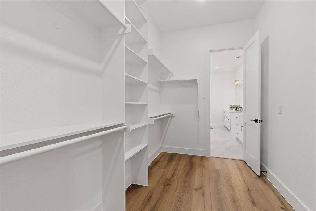 Walk-in closet featuring custom white shelving, integrated hanging rods, and wood-finish flooring