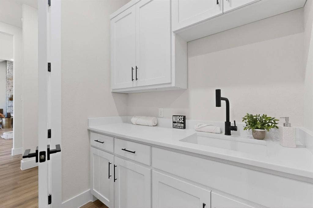 Shaker-style white cabinetry with matte black hardware, stone-surface countertop, integrated rectangular sink, and matte black gooseneck faucet