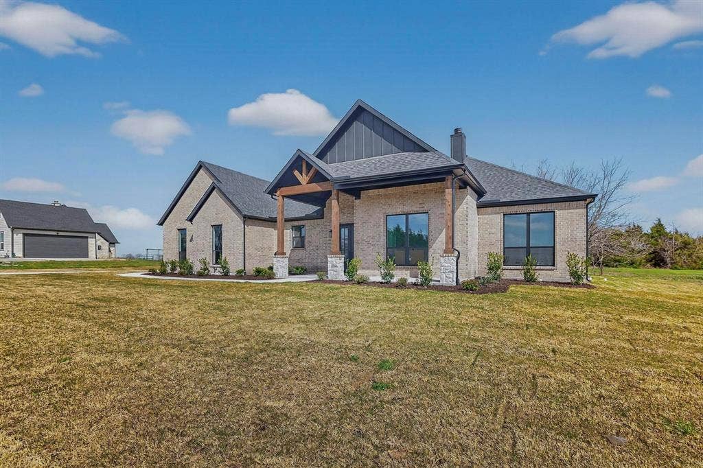 Custom brick and stone exterior featuring a covered front entry with timber accents, dark metal roof detailing, and black window frames