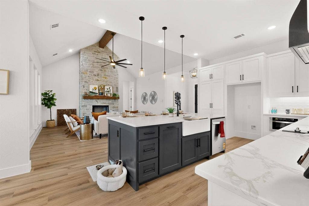 Kitchen featuring a central island with a farmhouse sink and stone-finish countertops, vaulted ceilings, stone-clad fireplace, and wood-finish flooring