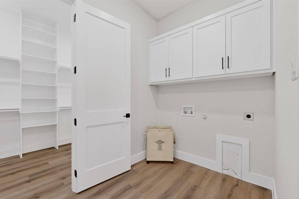 Laundry area featuring wood-finish flooring, white shaker-style cabinetry with matte black pulls, built-in shelving, and a two-panel interior door with matte black hardware