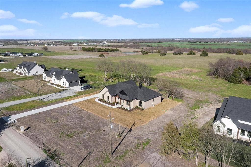 Single-story residence featuring a multi-gabled roofline, light-toned masonry exterior, concrete driveway, and expansive rear acreage