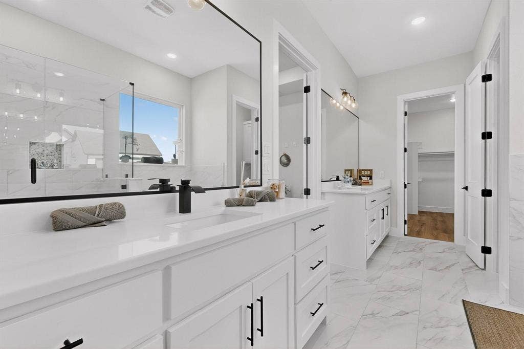Dual vanities featuring white cabinetry, quartz countertops, matte black fixtures, and large-scale framed mirrors, complemented by stone-patterned tile flooring