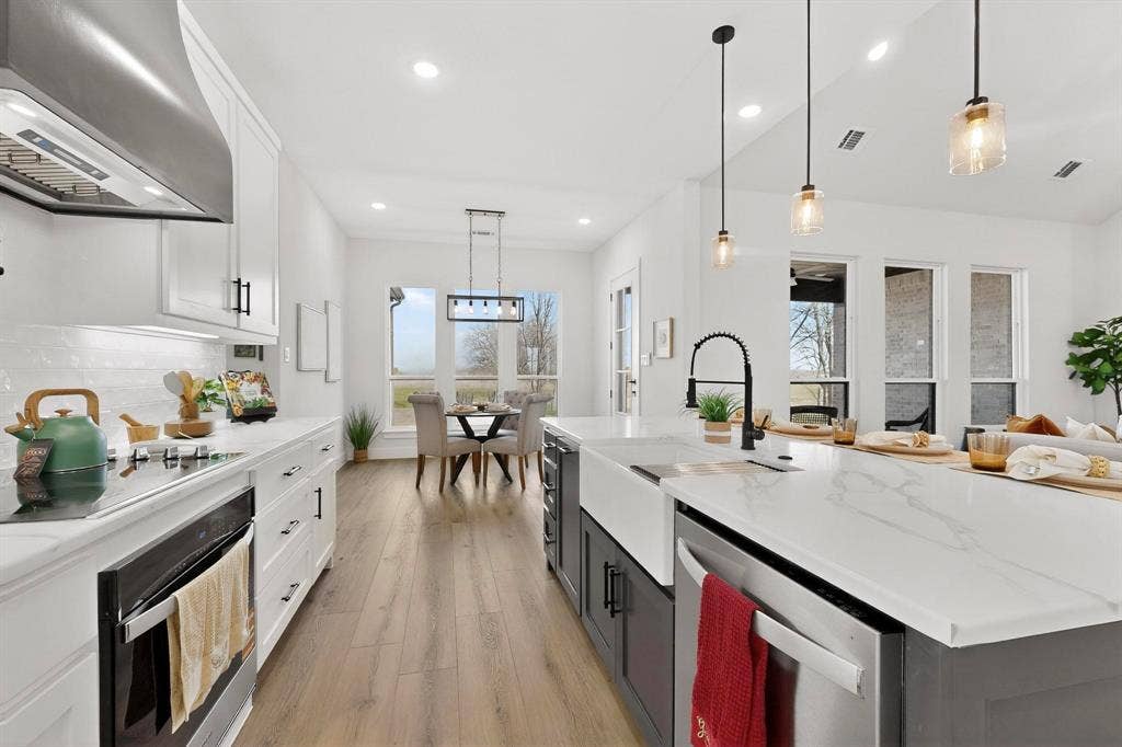 Kitchen featuring white shaker-style cabinetry, quartz countertops with a veined pattern, wood-finish flooring, a farmhouse-style apron sink, and a stainless steel range hood
