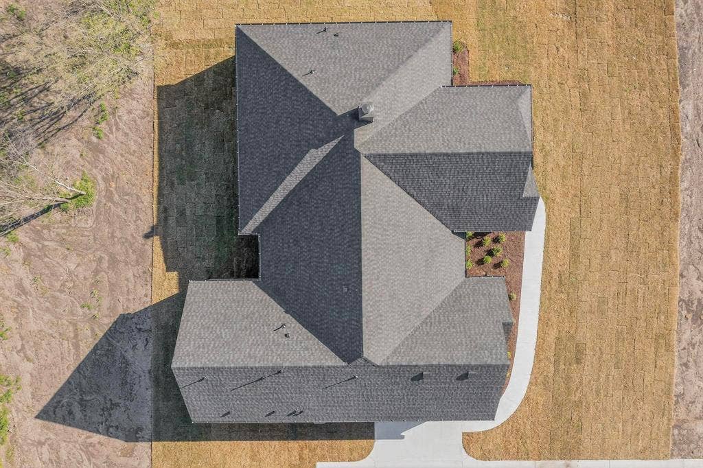 Aerial perspective featuring a multi-pitched roofline with asphalt shingles, a centered chimney stack, and a concrete walkway
