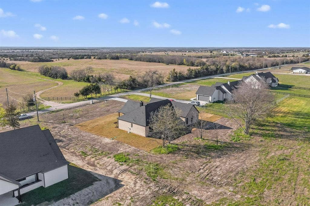 Aerial perspective featuring a multi-gabled roofline, brick exterior, paved driveway, and expansive acreage