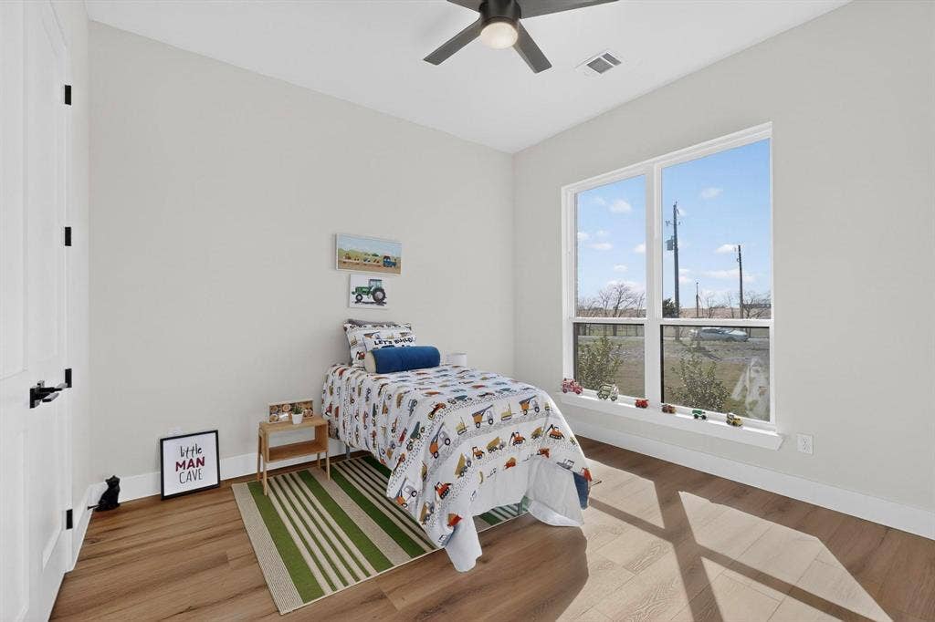 Neutral-toned interior featuring wood-finish flooring, a ceiling fan with integrated lighting, and large windows with a wide ledge